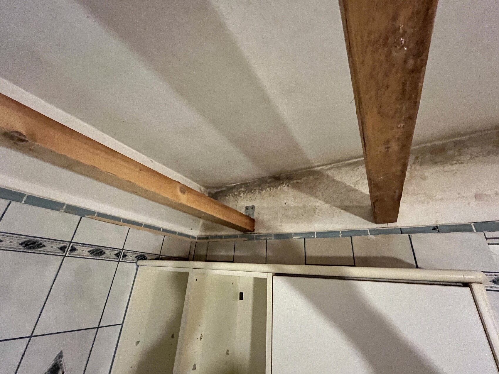 Badezimmerboden mit Fliesen, sichtbare Holzbalken und Feuchtigkeit an der Wand