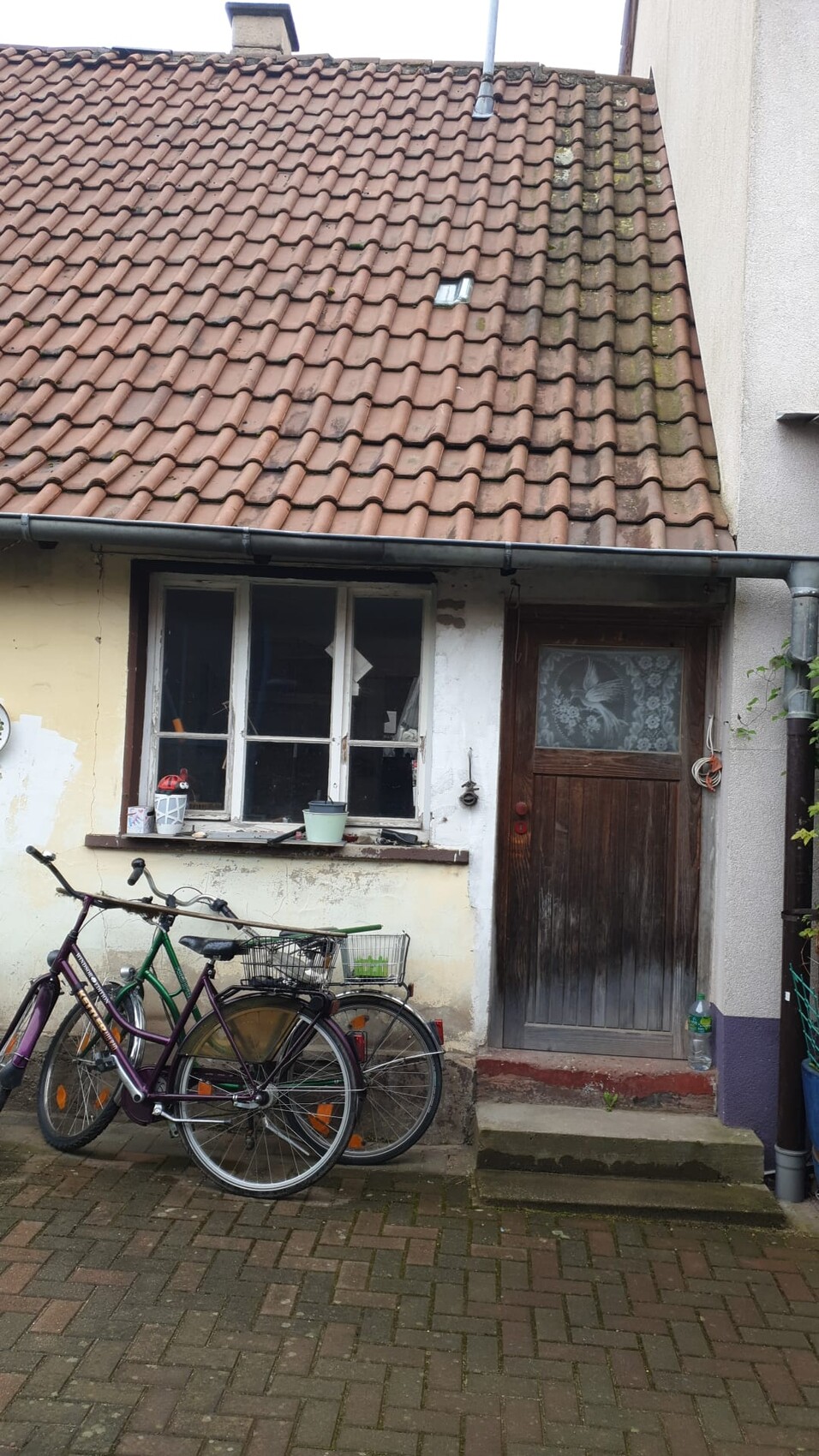 Vorderansicht eines Altbaus mit rotem Ziegeldach, Fenster und Holztür; davor zwei Fahrräder.