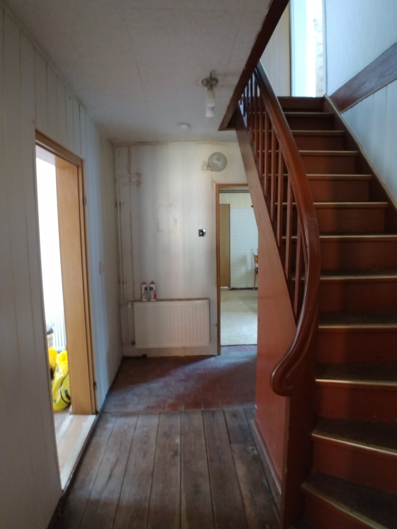 Heller Flur mit einer Holztreppe rechts, weißen Wänden, Heizkörper, und dunklem Holzboden.