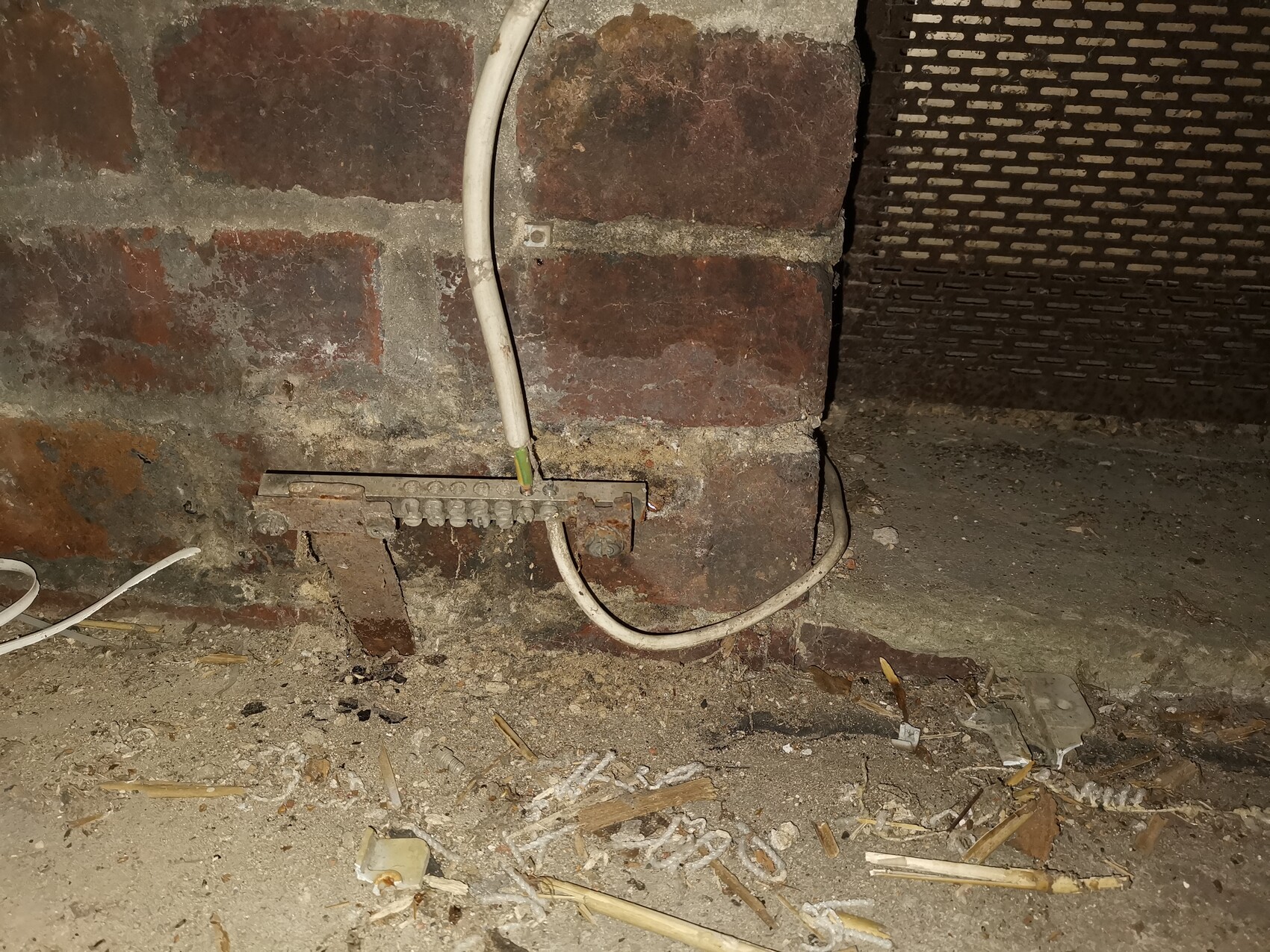Klemmenleiste an Ziegelwand im Keller, lose Kabel, Staub und Schutt.
