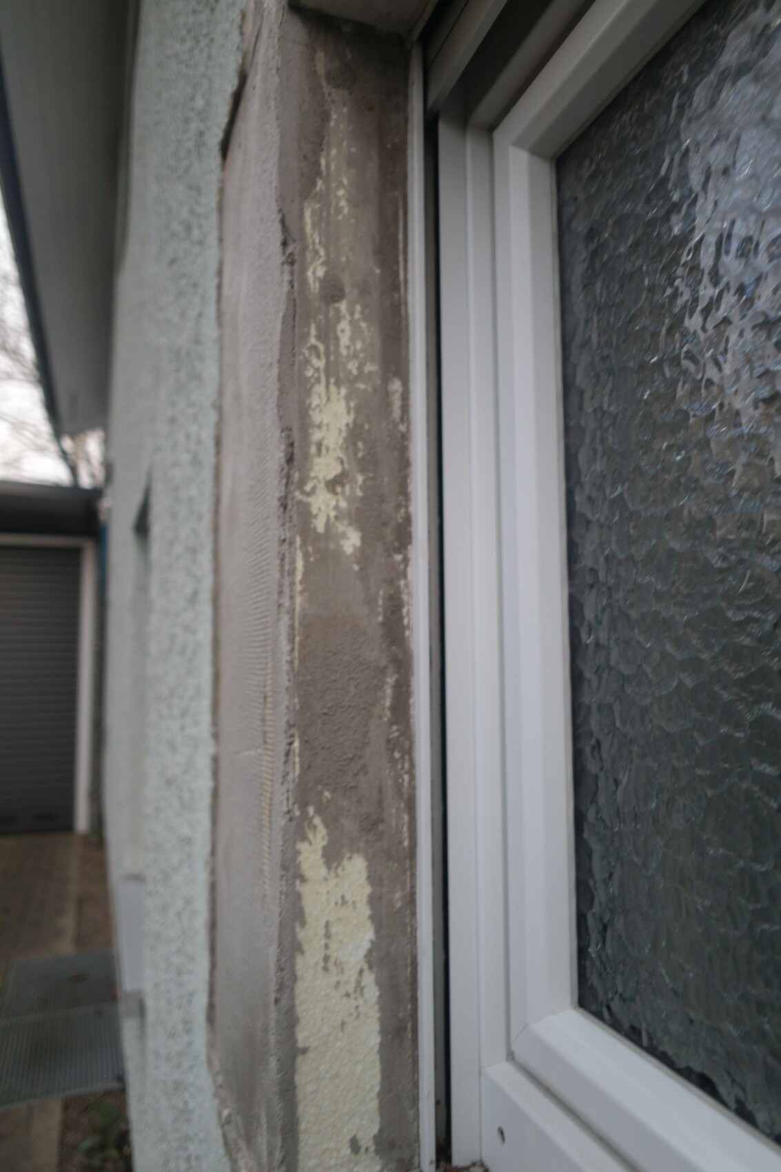 Nahaufnahme eines Fensterrahmens neben Wand mit abblätternder Farbe und strukturiertem Glas