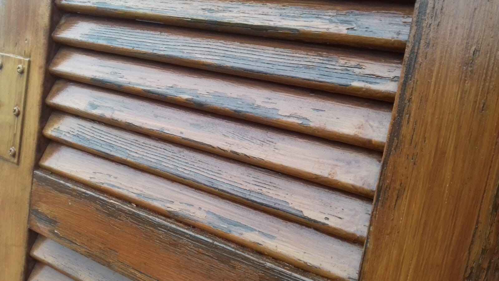 Verwitterte Holzlamellen mit abblätternder Farbe an einer Tür.