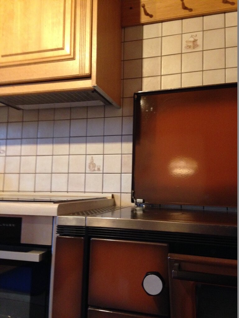 Küche mit braunen Holzschränken, Fliesenwand, Ofen und Herd in älterem Stil.