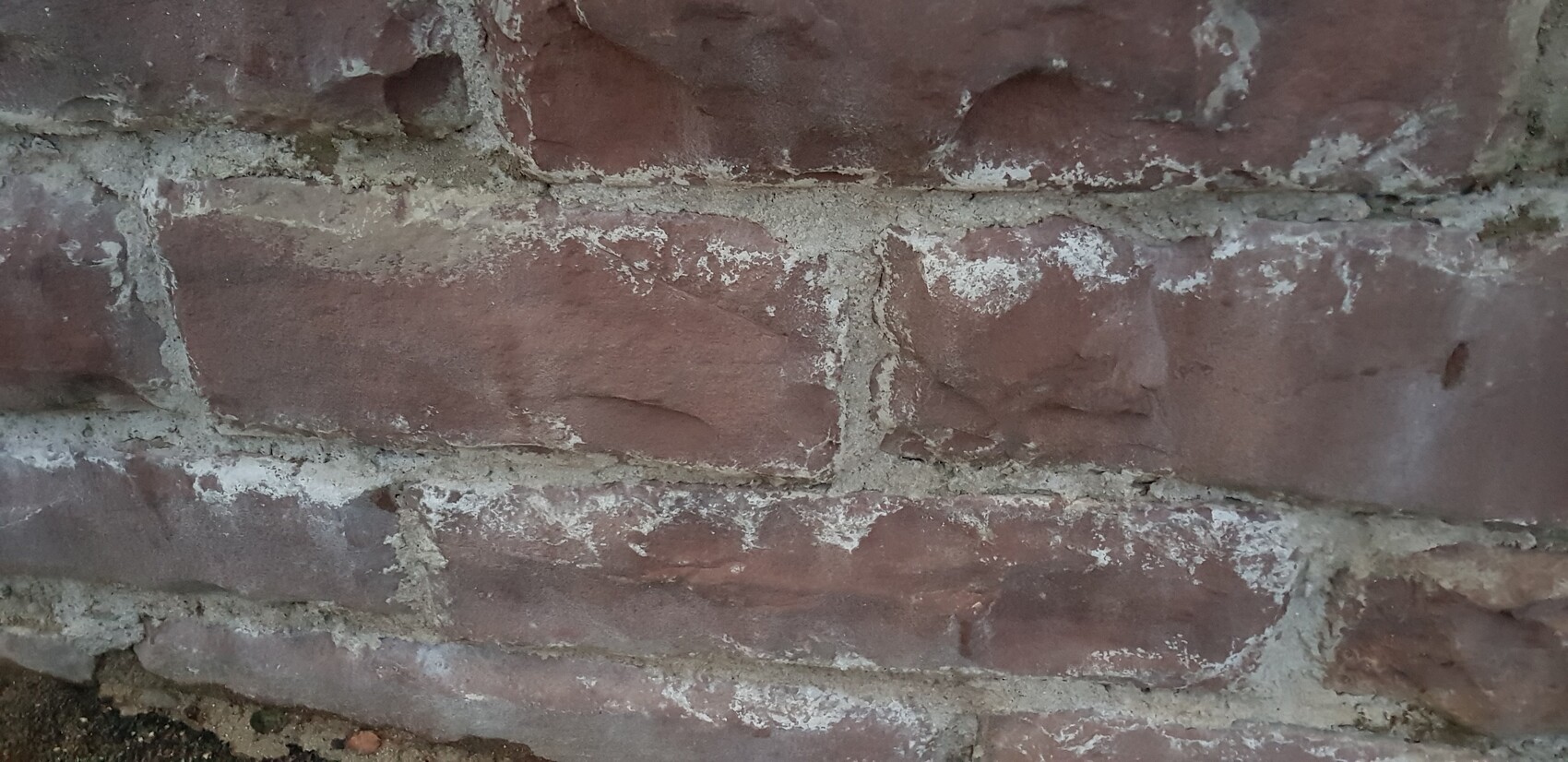 Nahaufnahme einer roten Ziegelwand mit weißem Mörtel und Kalkflecken.