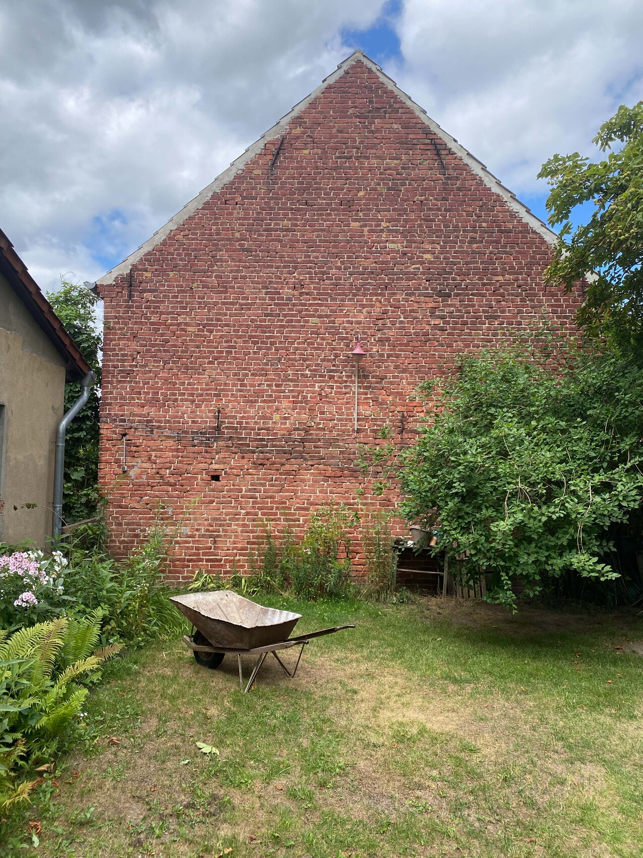 Rote Backsteinwand eines Hauses mit Giebeldach; Garten mit Schubkarre im Vordergrund