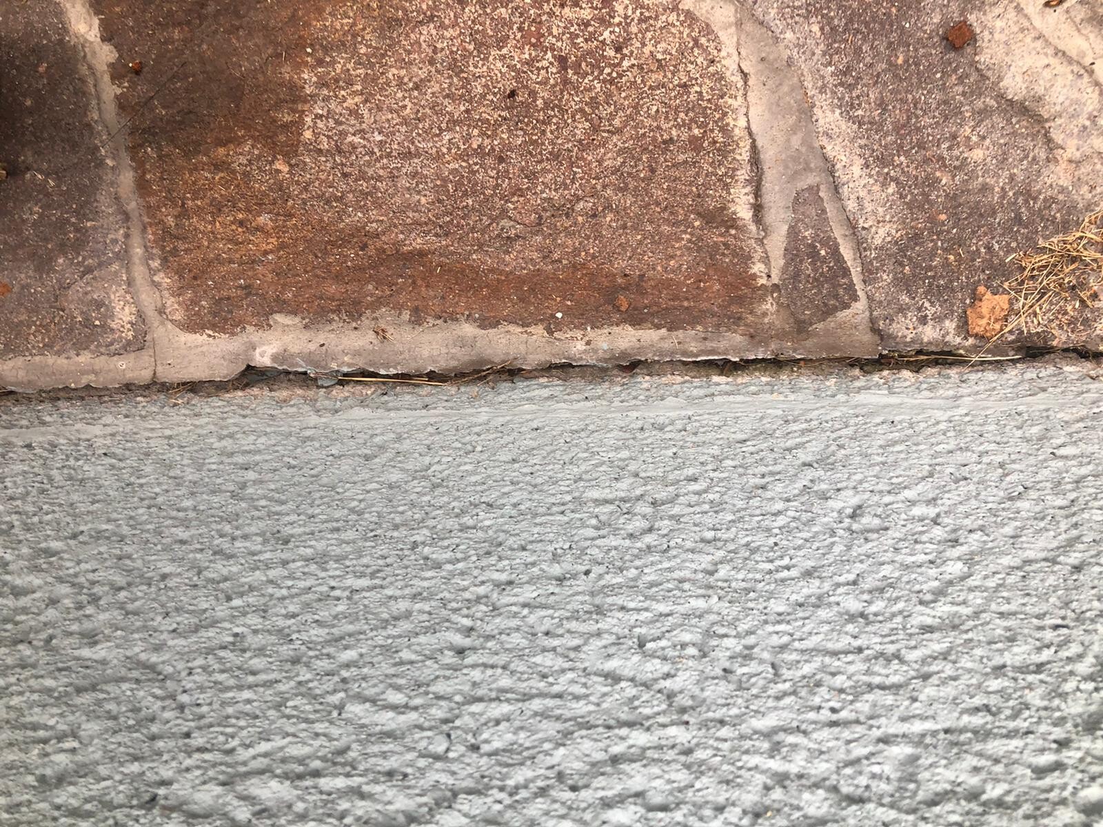 Braune Steinplatten über grauer, rauer Betonfläche mit Fugenlinie.