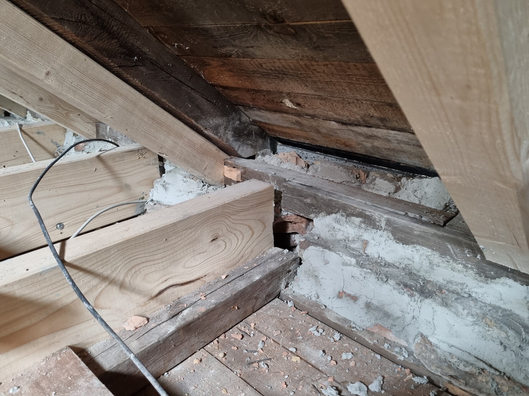 Dachboden mit Holzbalken, Ziegelresten, Mörtel und Staub; lose Kabel über Balken.