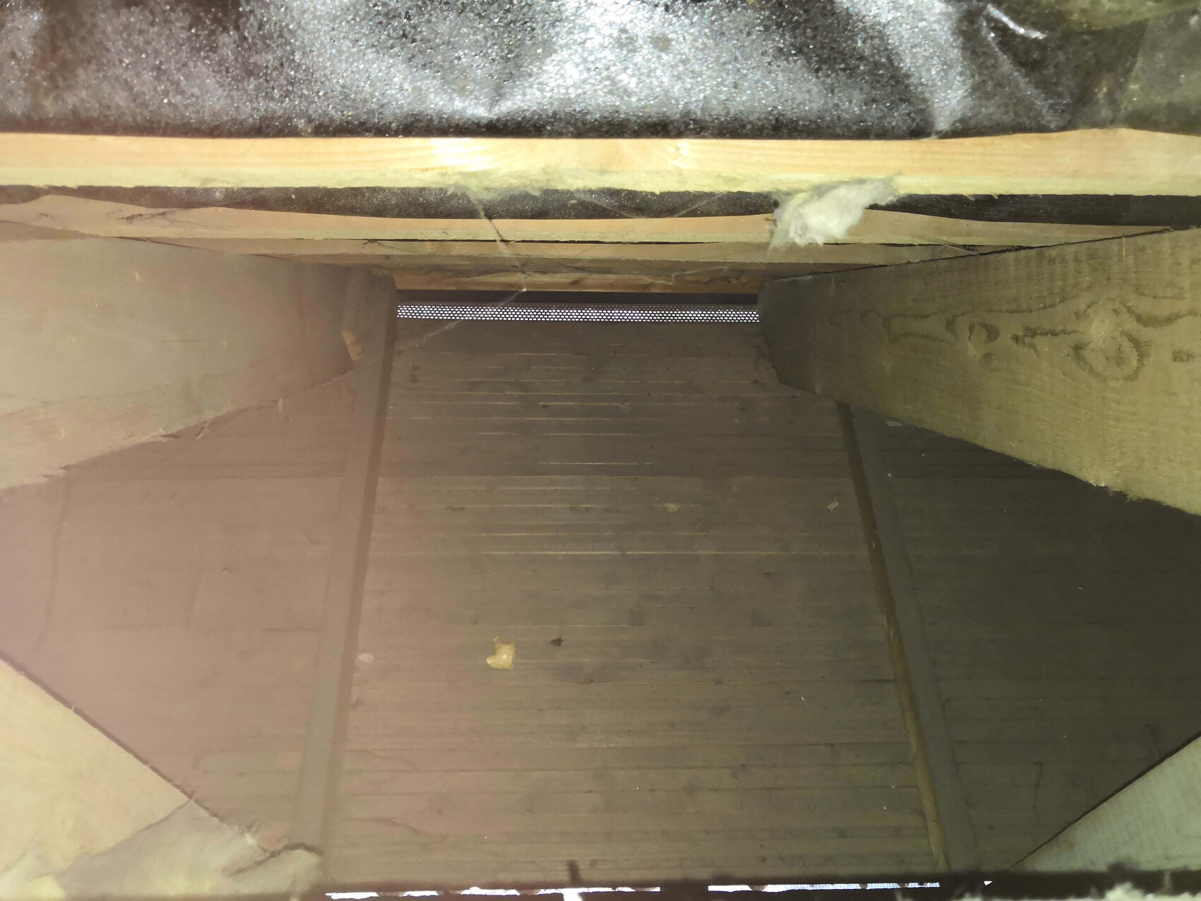 Dachbodenraum mit Holzboden, Balken und Dämmung; Staub und Licht am fernen Ende.