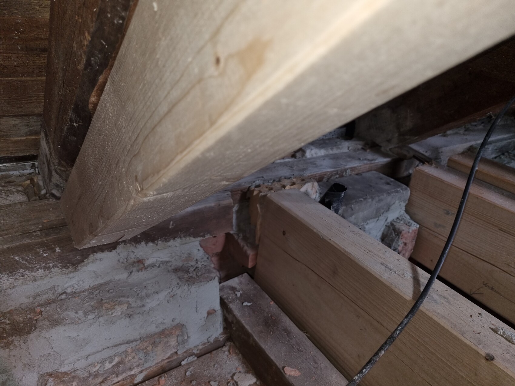 Dachboden mit schrägem Holzbalken, Holzbohlen, Ziegelresten, Staub und ein Kabel.