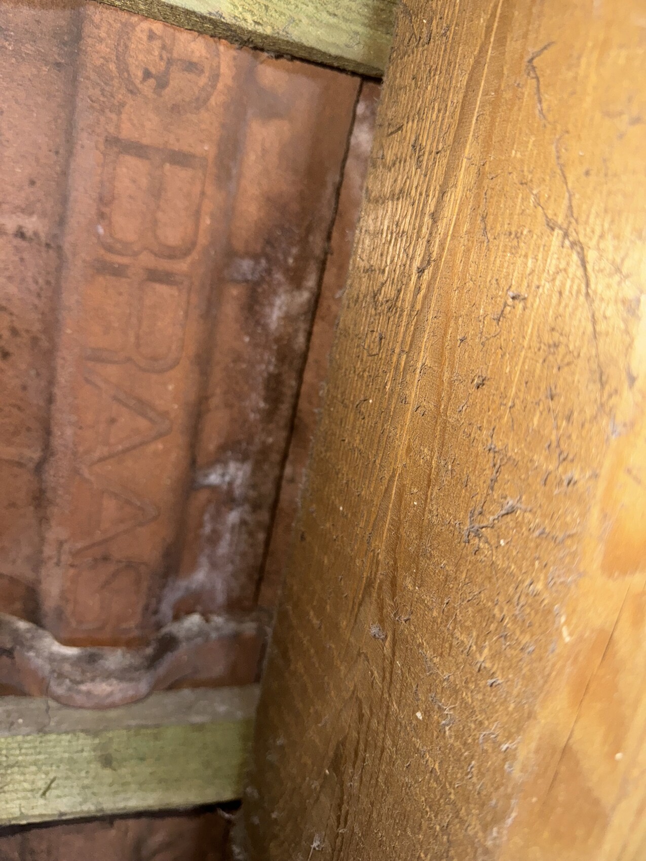 Nahaufnahme eines braunen Holzbalkens neben einer rötlichen Backsteinwand mit Staub und Schmutz.