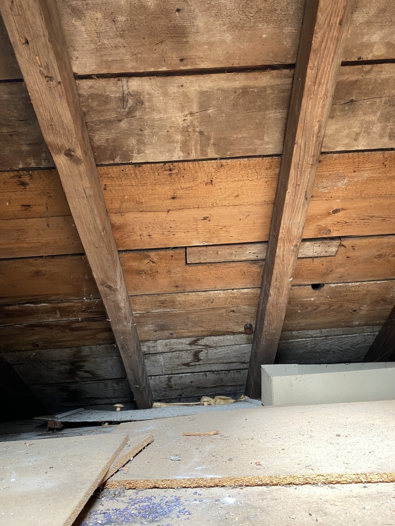 Dachboden mit sichtbaren Holzbalken, Holzplatten und Staub auf dem Boden.
