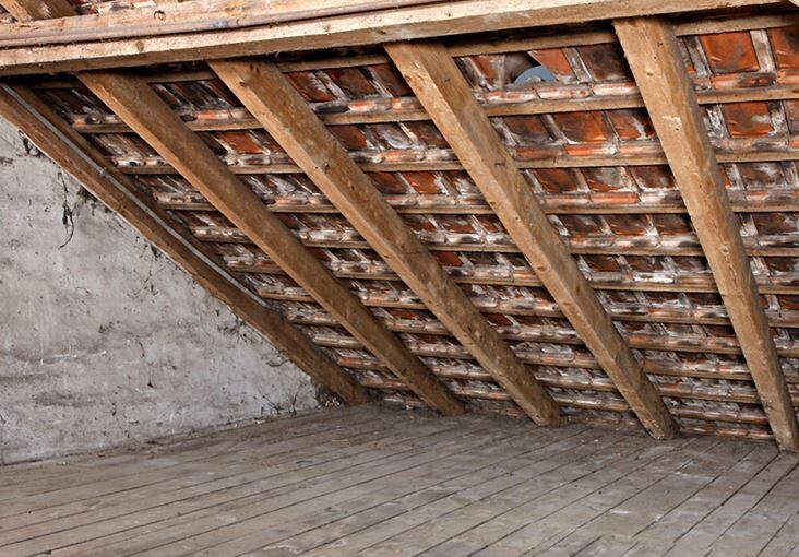 Dachboden mit freigelegter Holzbalkenkonstruktion und Steinwand im Hintergrund.