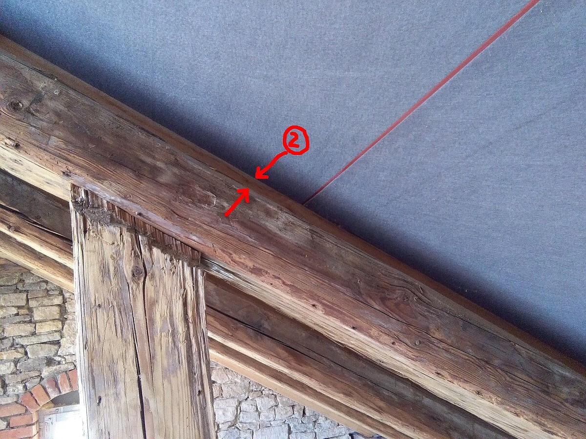 Alte Holzbalkenkonstruktion im Dachstuhl neben Steinwand und blauer Dämmung