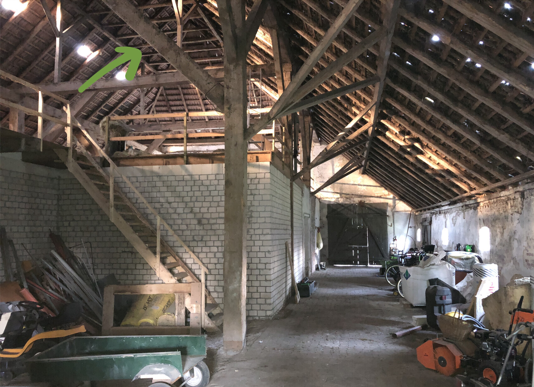 Rustikale Scheune: Holzträger, Treppe zum Loft, Gegenstände und Werkzeuge im Innenraum.