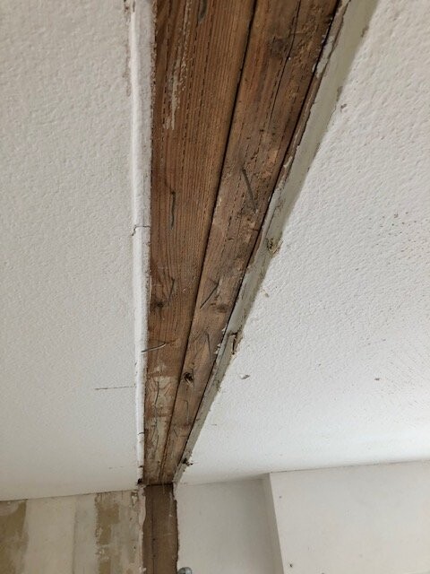 Freigelegter Holzbalken in einer verputzten Decke mit Rissen