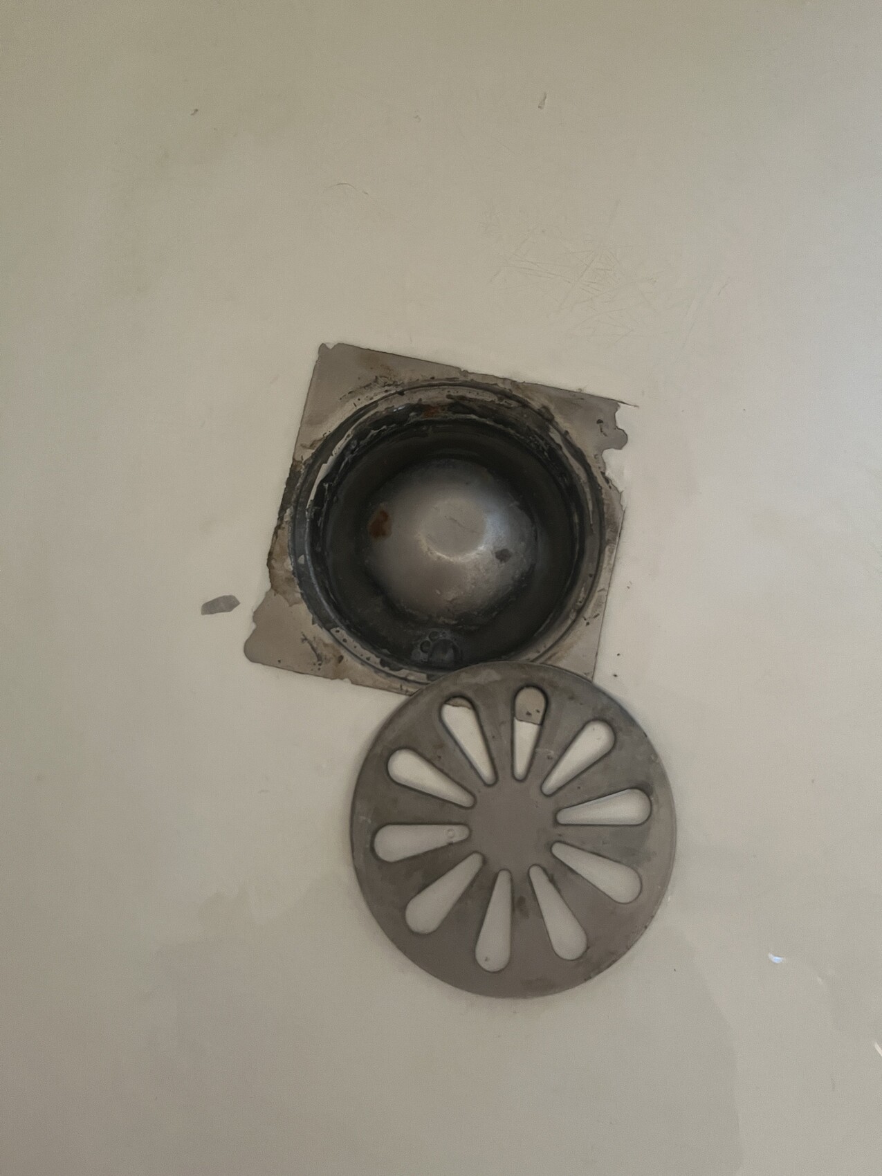 Offener Badablauf: runder Metalldeckel liegt neben dem Loch im Fliesenboden.