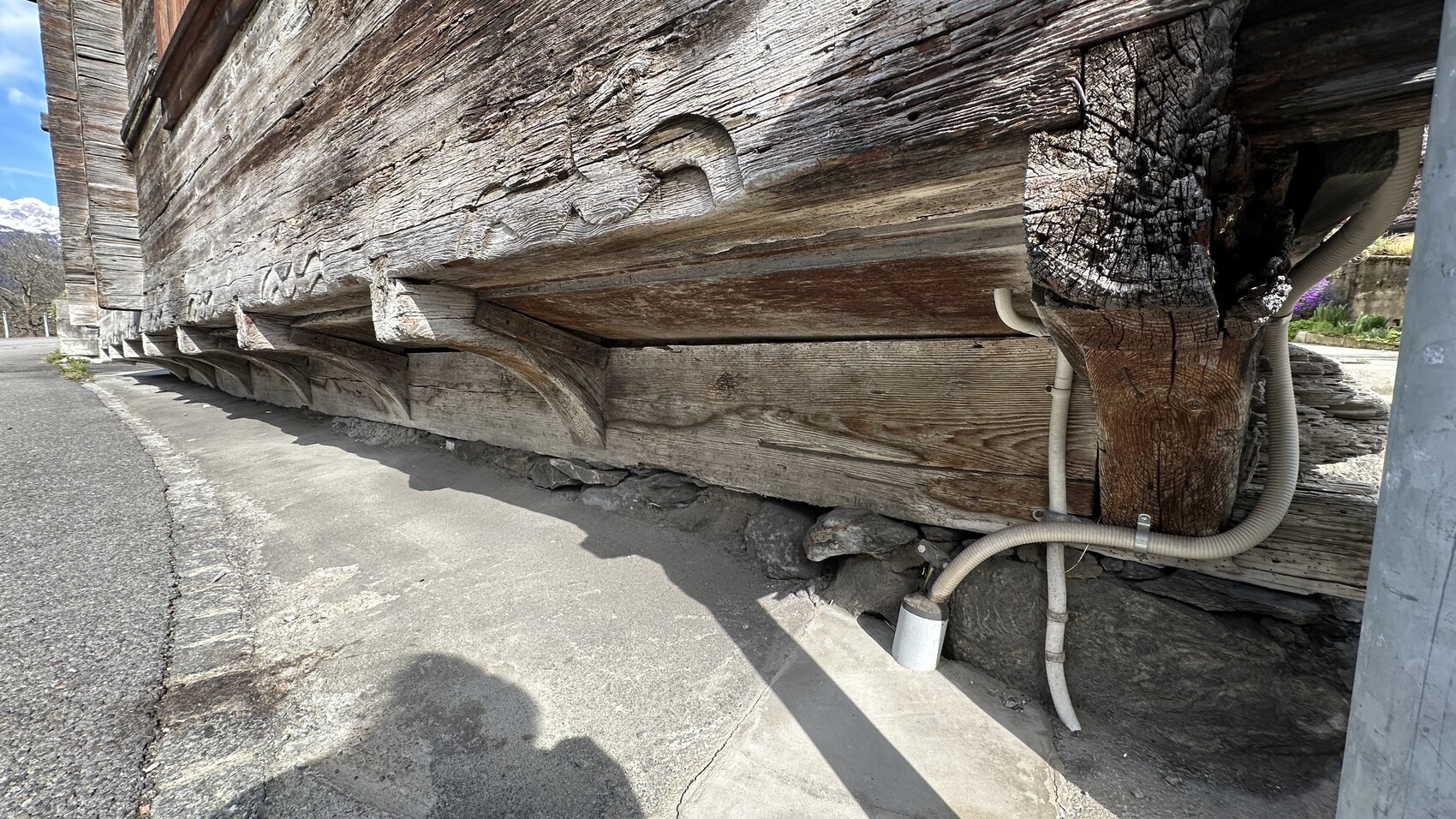 Nahaufnahme einer stark verwitterten Holzkonstruktion mit Balken, Kabeln und Steinfundament.