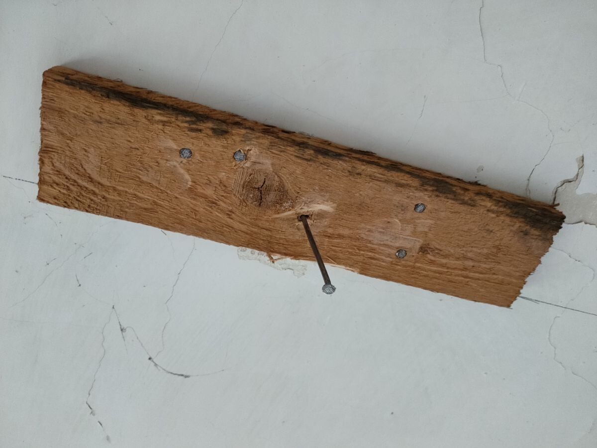 Alte Holzlatte mit mehreren Nägeln, rostig, liegt auf einer hellgrauen, rissigen Oberfläche.