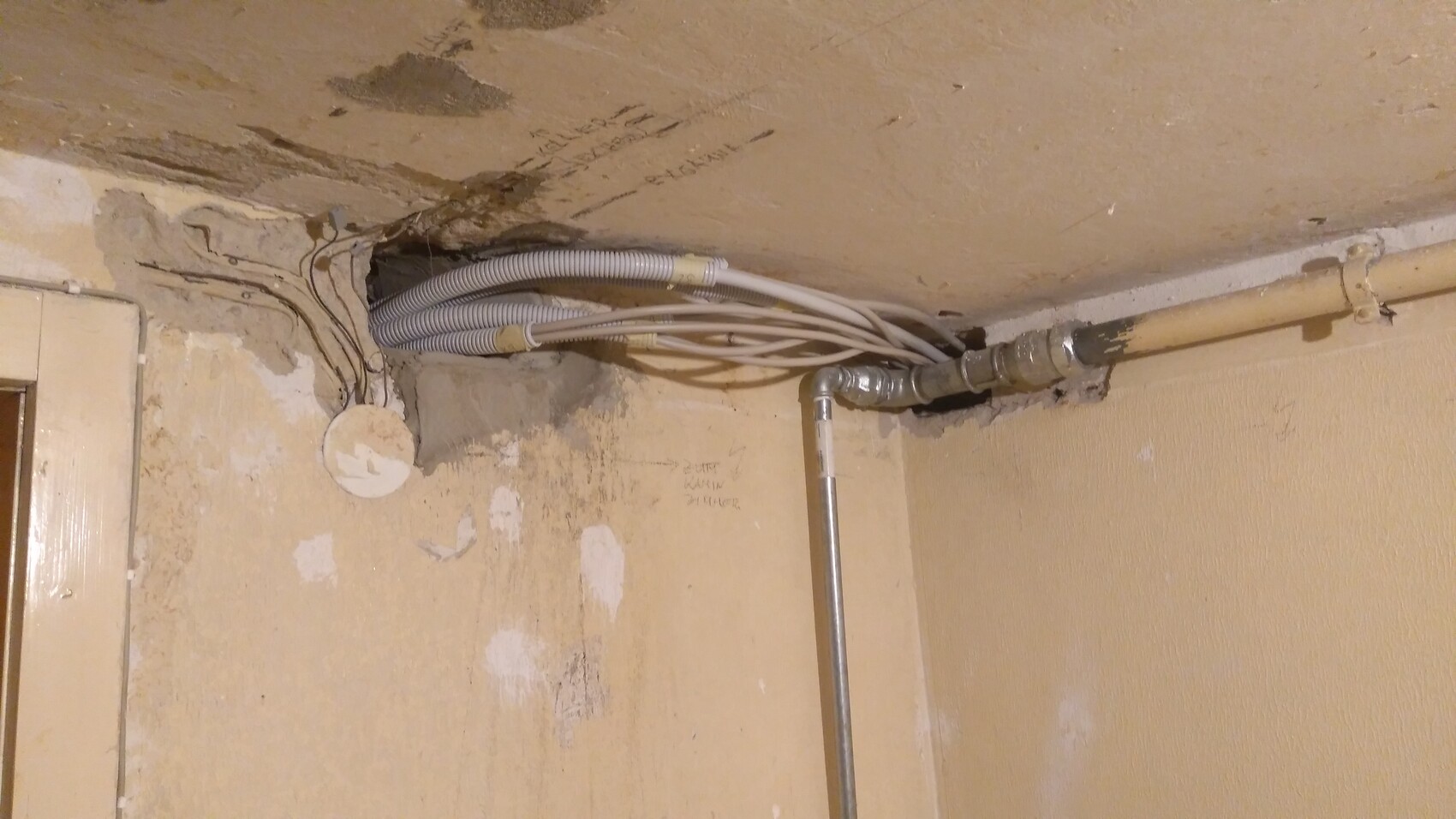 Kabelbündel in flexibler Leitung neben Metallrohren an verputzter Decke.