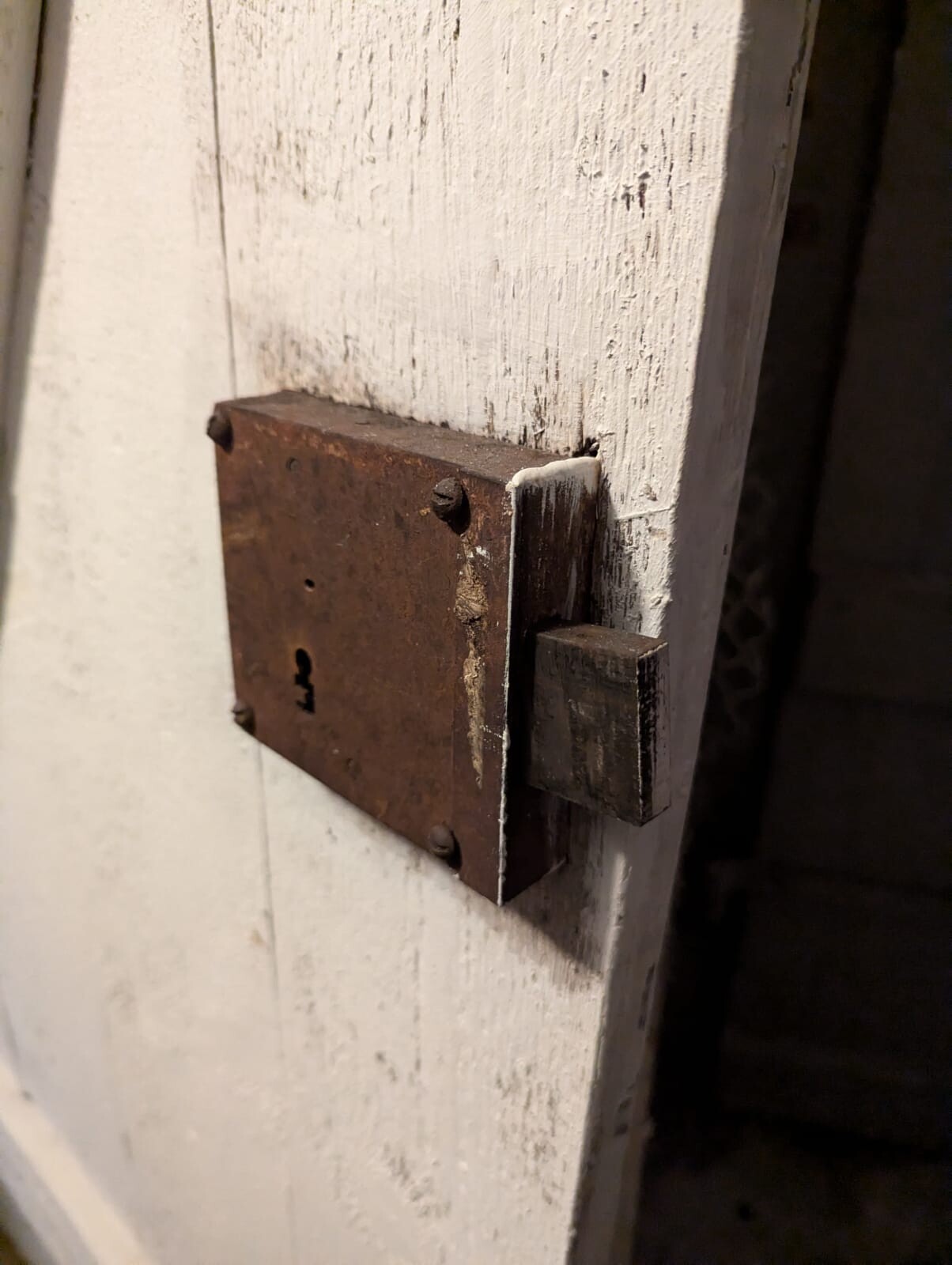 Rostige Metallplatte mit Riegel an einer weiß gestrichenen Holztür.