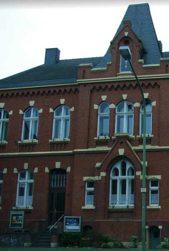 Rotes Backsteingebäude mit hohen Fenstern und Treppenaufgang, davor Straßenlampe