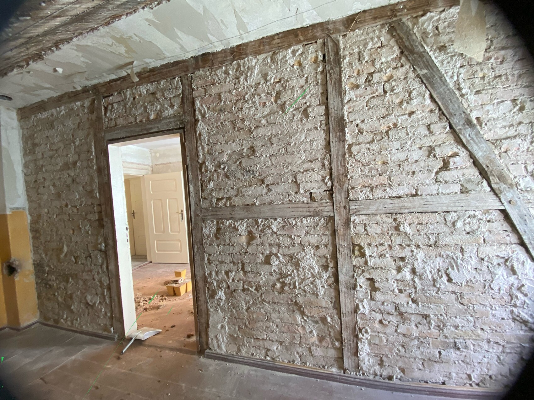 Rohes Mauerwerk mit Holzfachwerk und diagonaler Balkenkonstruktion; Türdurchgang zu einem Raum.