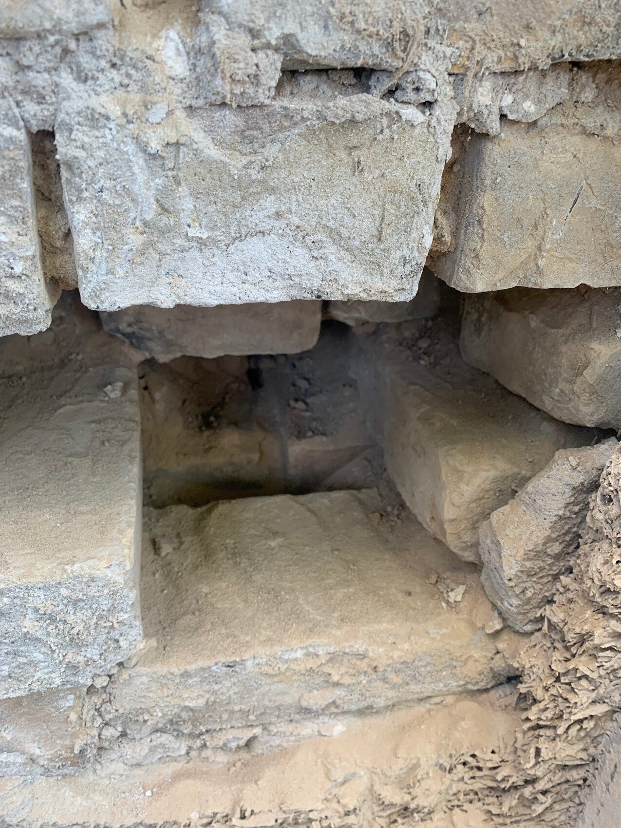 Rohsteinmauer mit kleinem dunklen Hohlraum zwischen Steinen, staubig.