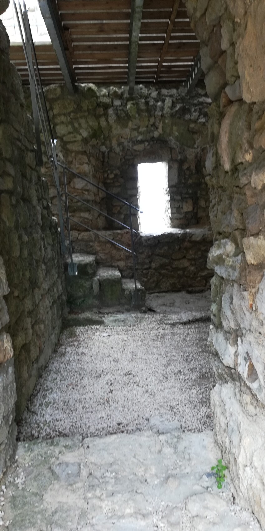 Innenansicht einer steinernen Ruine mit Treppe, Geländer und kleinem Fenster am Ende.