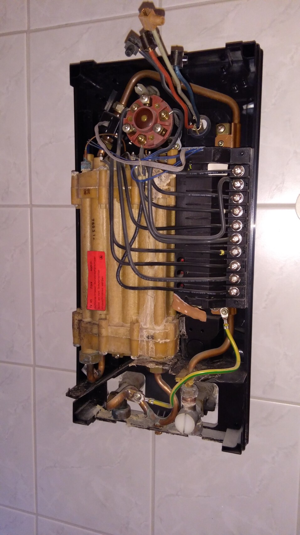 Offenes Elektrikpanel mit Schraubklemmen, rotem Rundklemmenblock, vielen Kabeln, Kupferrohren.