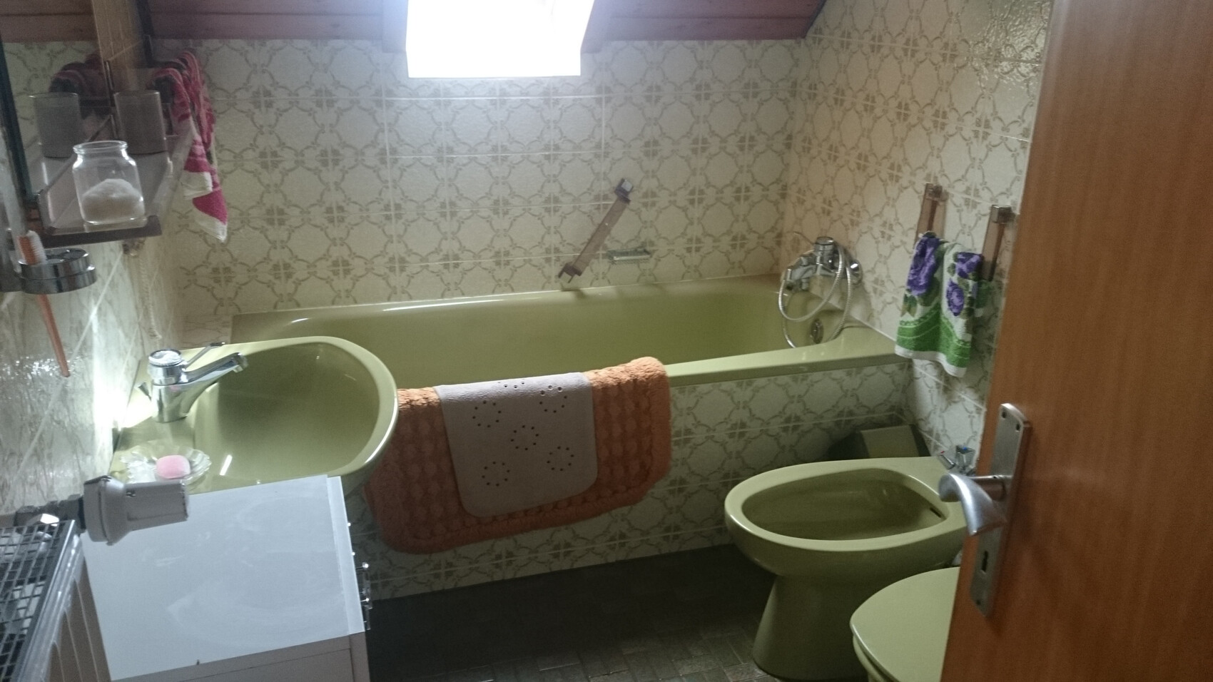 Altmodisches Badezimmer mit grünem Waschbecken, grünem Badewanne und gemusterten Wandfliesen.