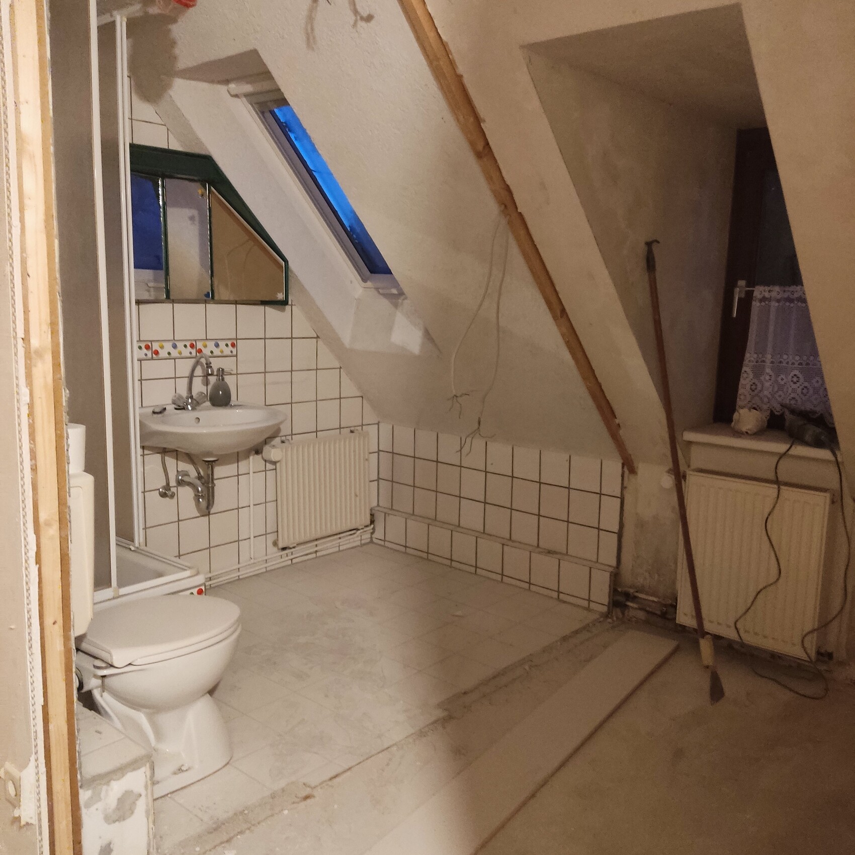 Dachgeschoss-Badezimmer mit WC, Waschbecken, Heizkörper, schrägem Dachfenster und Fliesen.