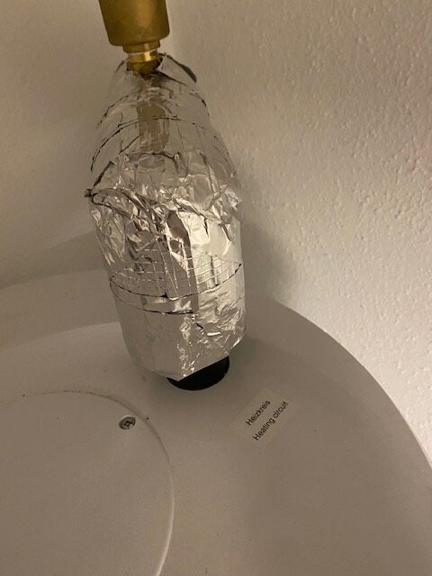 Aluminiumfolie umwickelter Gegenstand ragt aus einer runden Öffnung eines weißen Geräts.