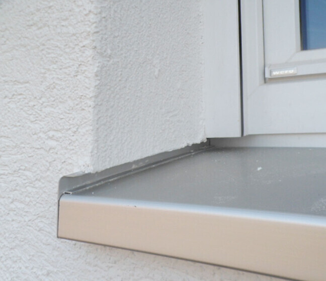 Außenfensterbank aus Metall vor weißer verputzter Wand.