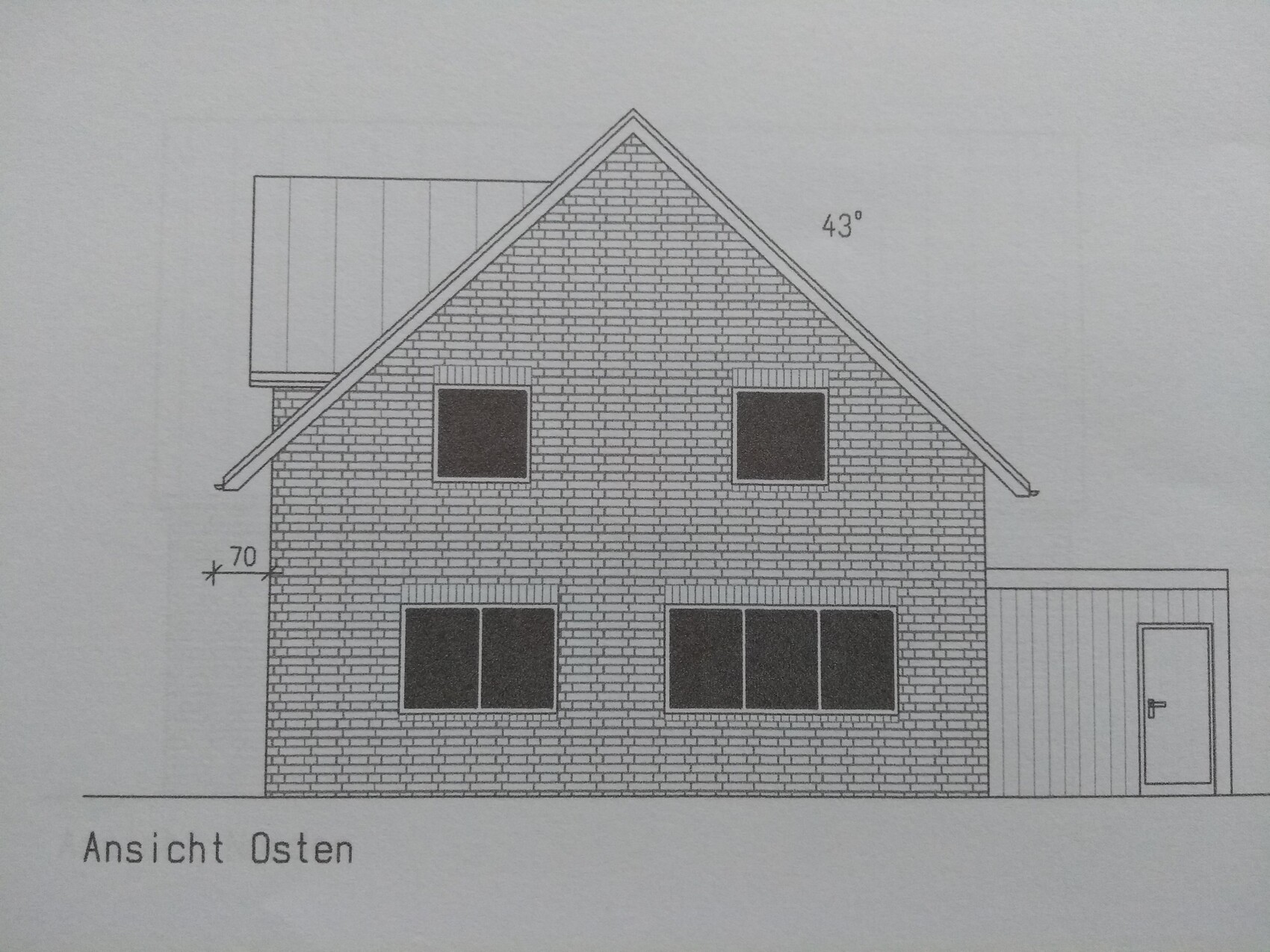 Ostansicht eines zweistöckigen Ziegelhauses mit Satteldach und rechts anliegendem Anbau mit Tür.