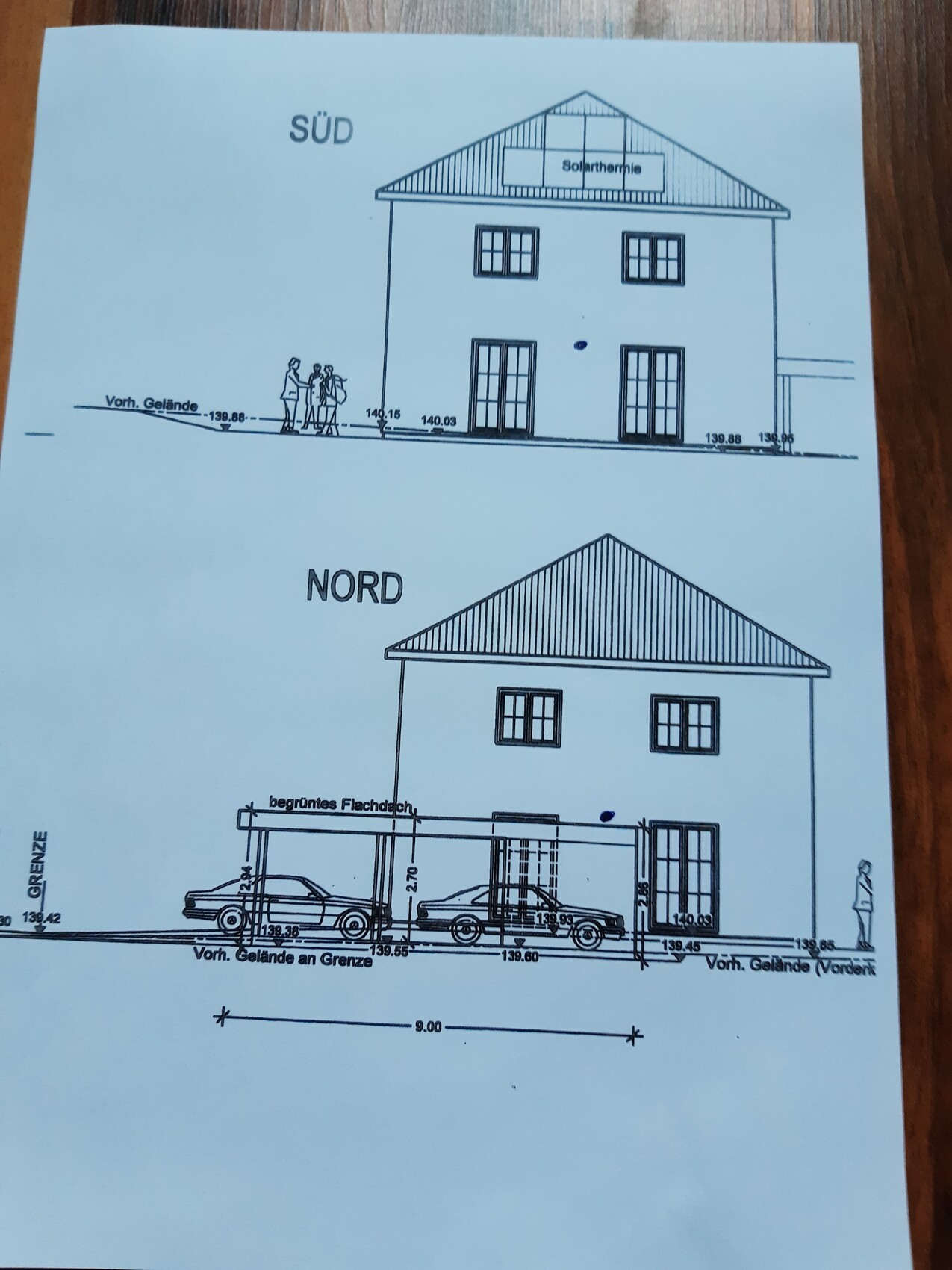 Zweistöckiges Haus mit Solarthermie-Dach (SÜD); Nordansicht mit Carport und Autos.