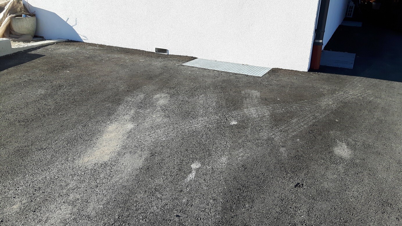 Außenbereich eines Hauses mit asphaltiertem Vorplatz und Metallrost auf dem Boden