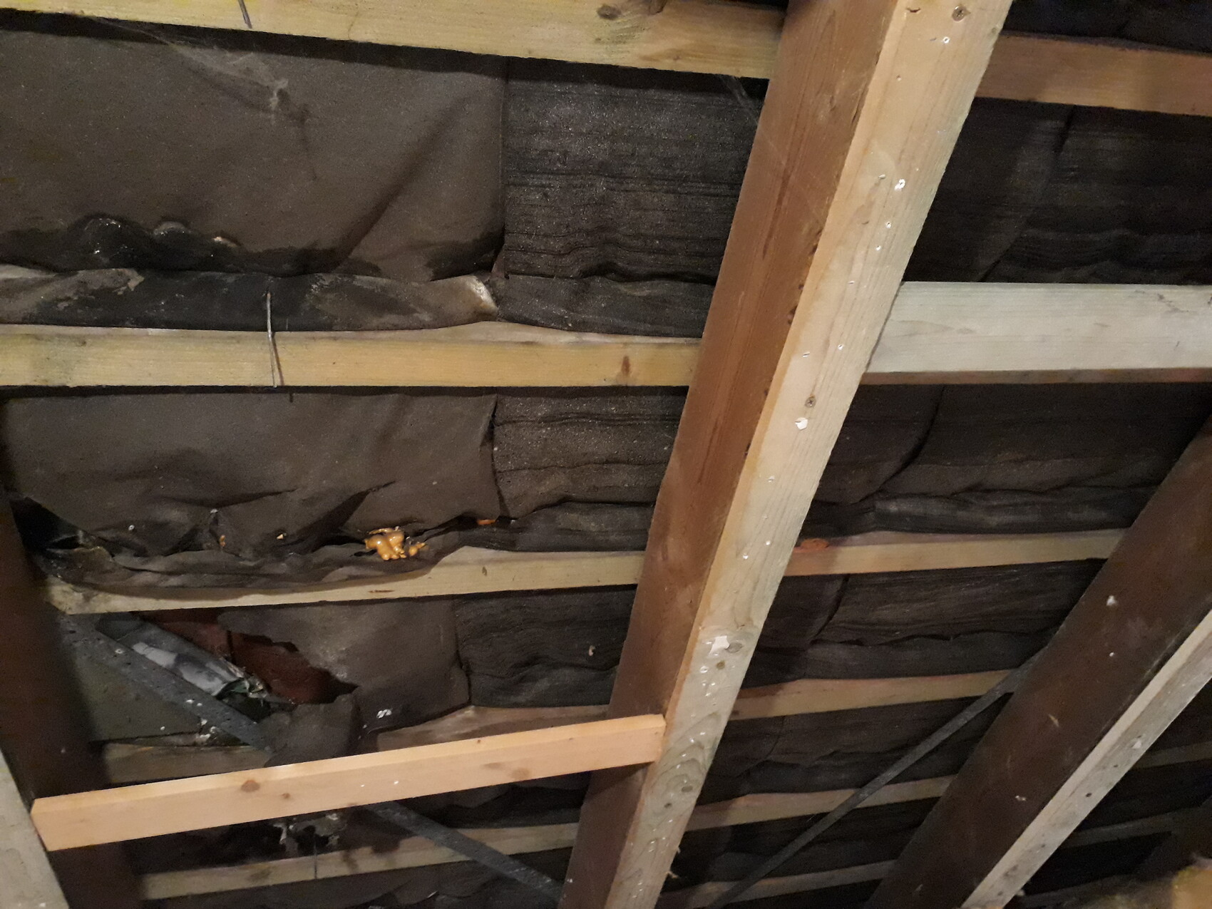 Dachboden mit Holzbalken und dunkler Dämmung zwischen Sparren