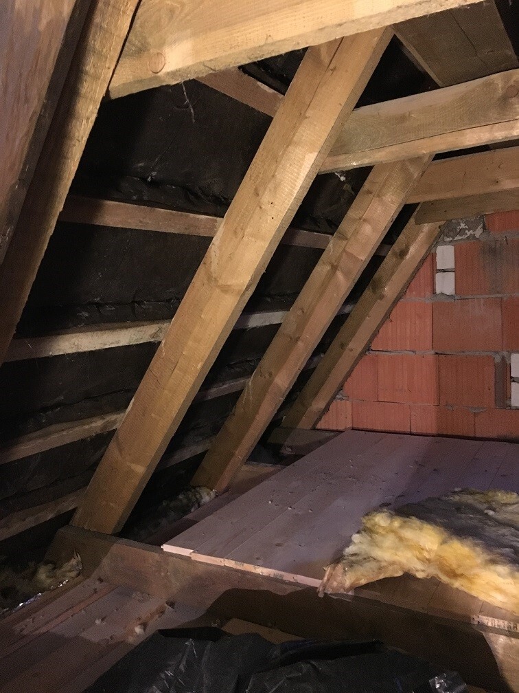 Dachboden mit Holzbalken, Dachstuhl, Dämmung und roher Ziegelwand sichtbar.