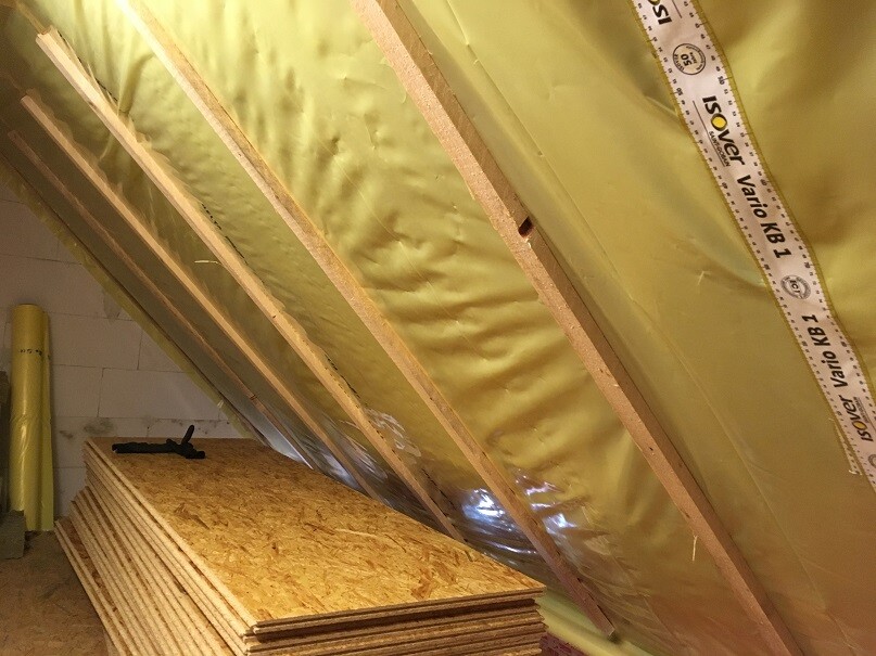 Spitzboden mit gelber Dämmfolie, Holzlatten und gestapelten OSB-Platten.