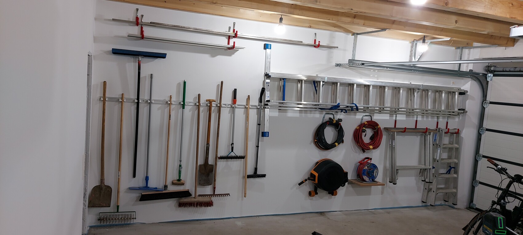 Ordentliche Garage mit Werkzeugwand: Schaufeln, Besen, Leiter, Schläuche und Kabel.