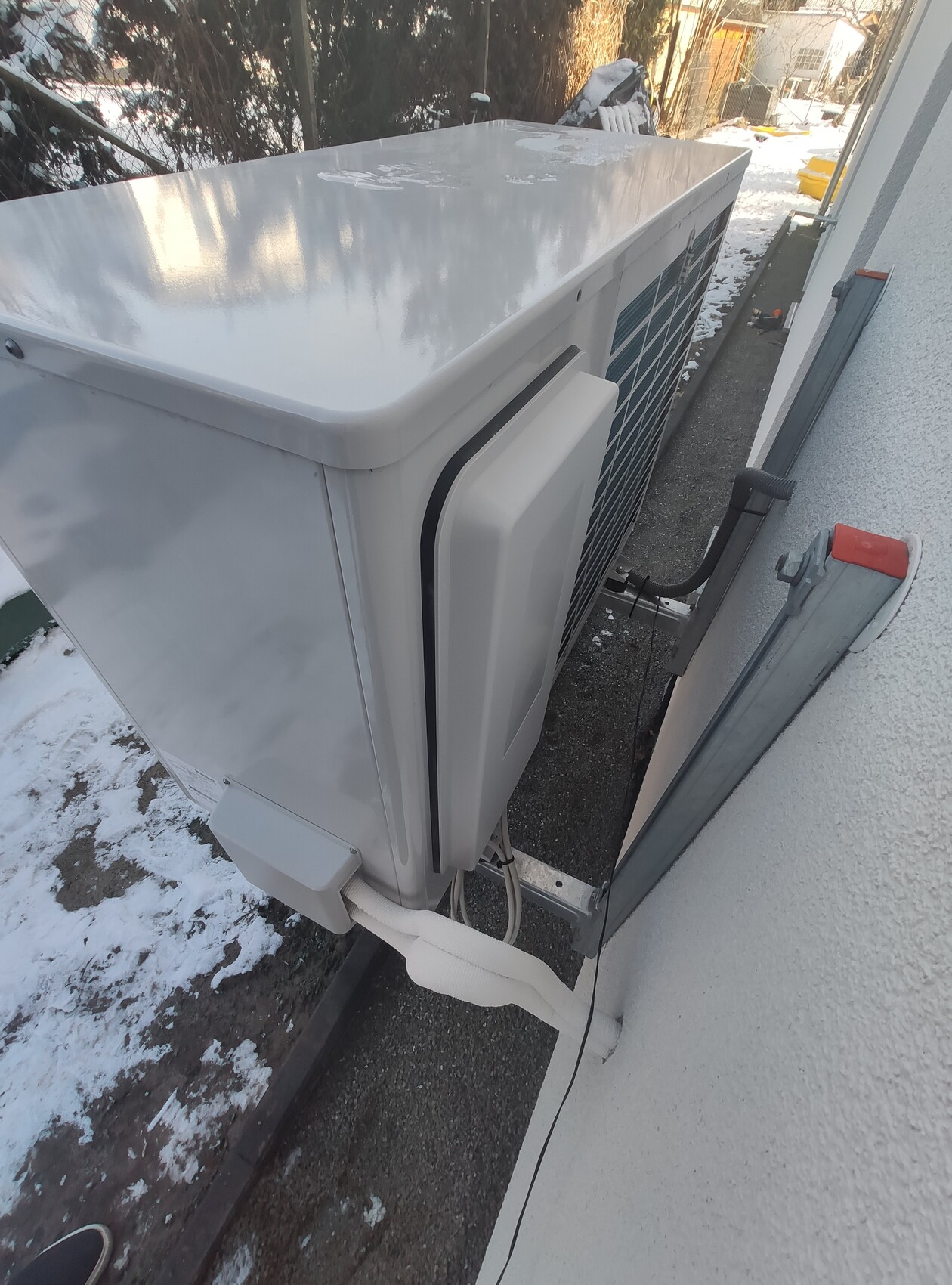Außenkondensator einer Klimaanlage an der Hauswand, isolierte Rohre, Schnee rundherum.