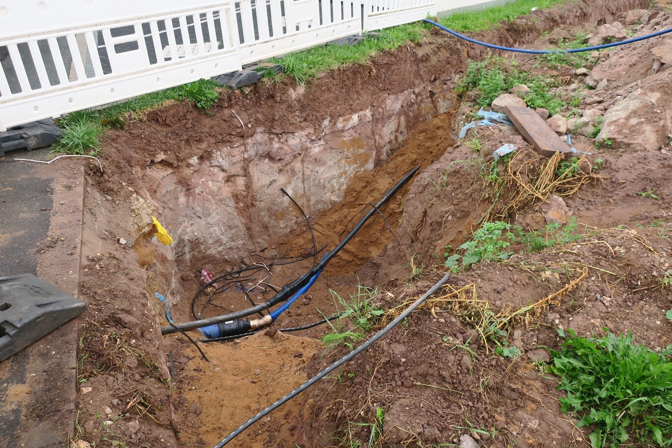 Ausgehobene Baugrube im Garten mit Rohren und Kabeln für Bauarbeiten