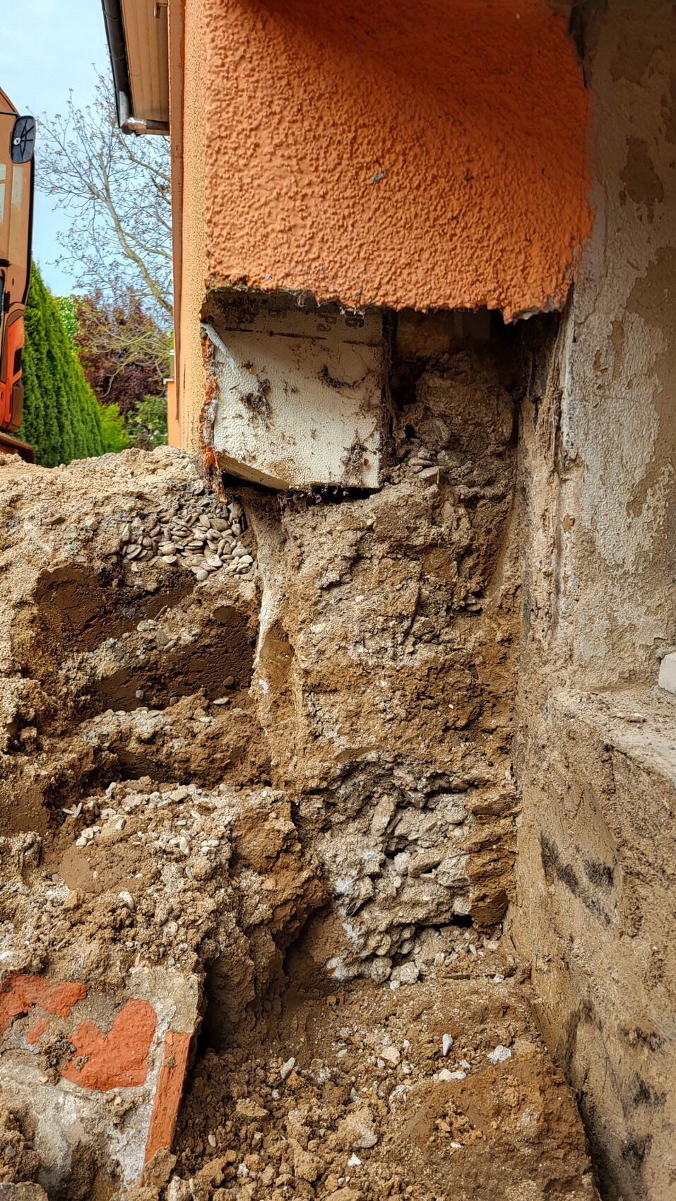 Ausgehobene Baugrube neben roter Putzwand, Schutt und Betonreste.