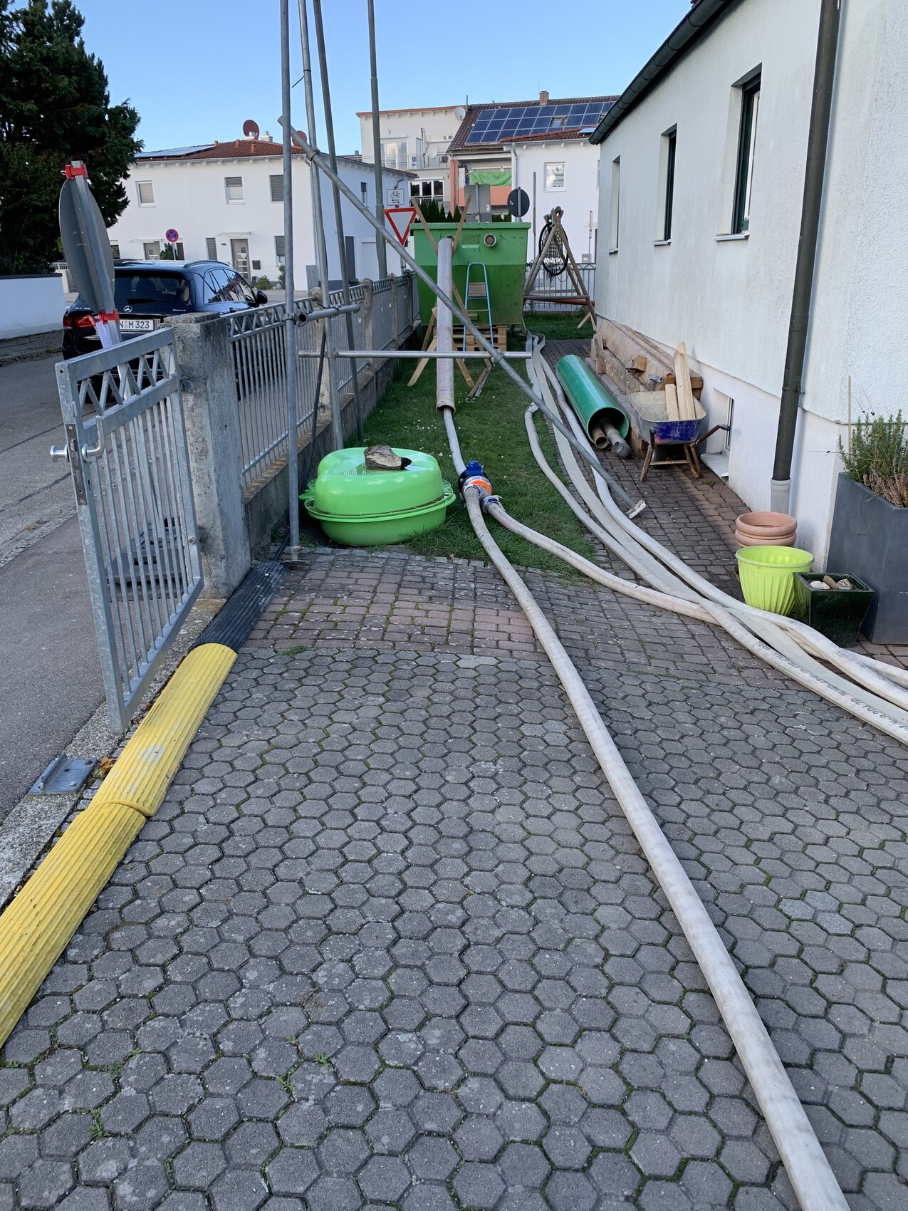 Außenbereich eines Gebäudes mit langen Schläuchen, grünem runden Tank und Baumaterialien.