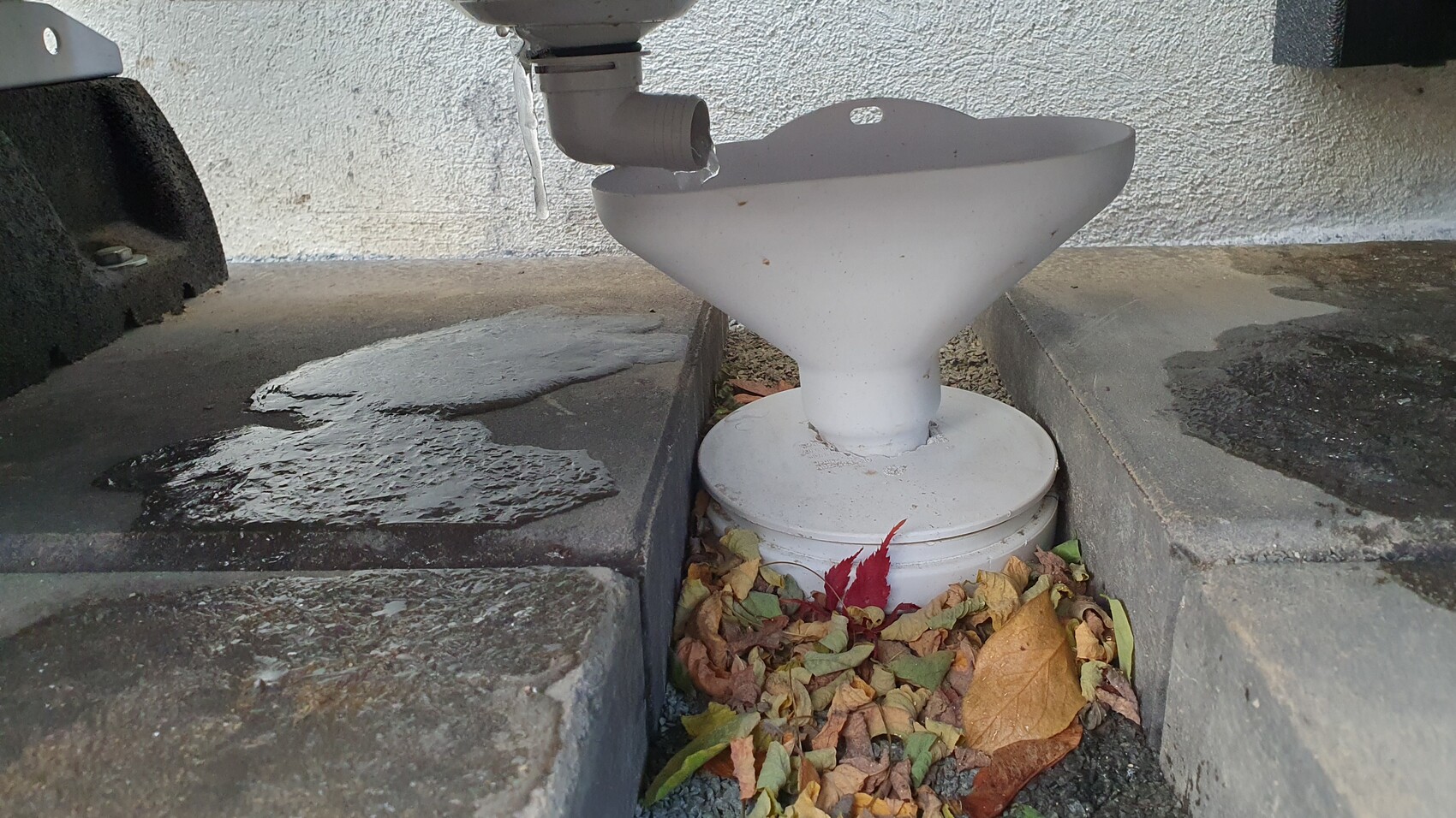 Weiße Trichter-Säule mit Abflussrohr zwischen Steinplatten, Herbstlaub darunter