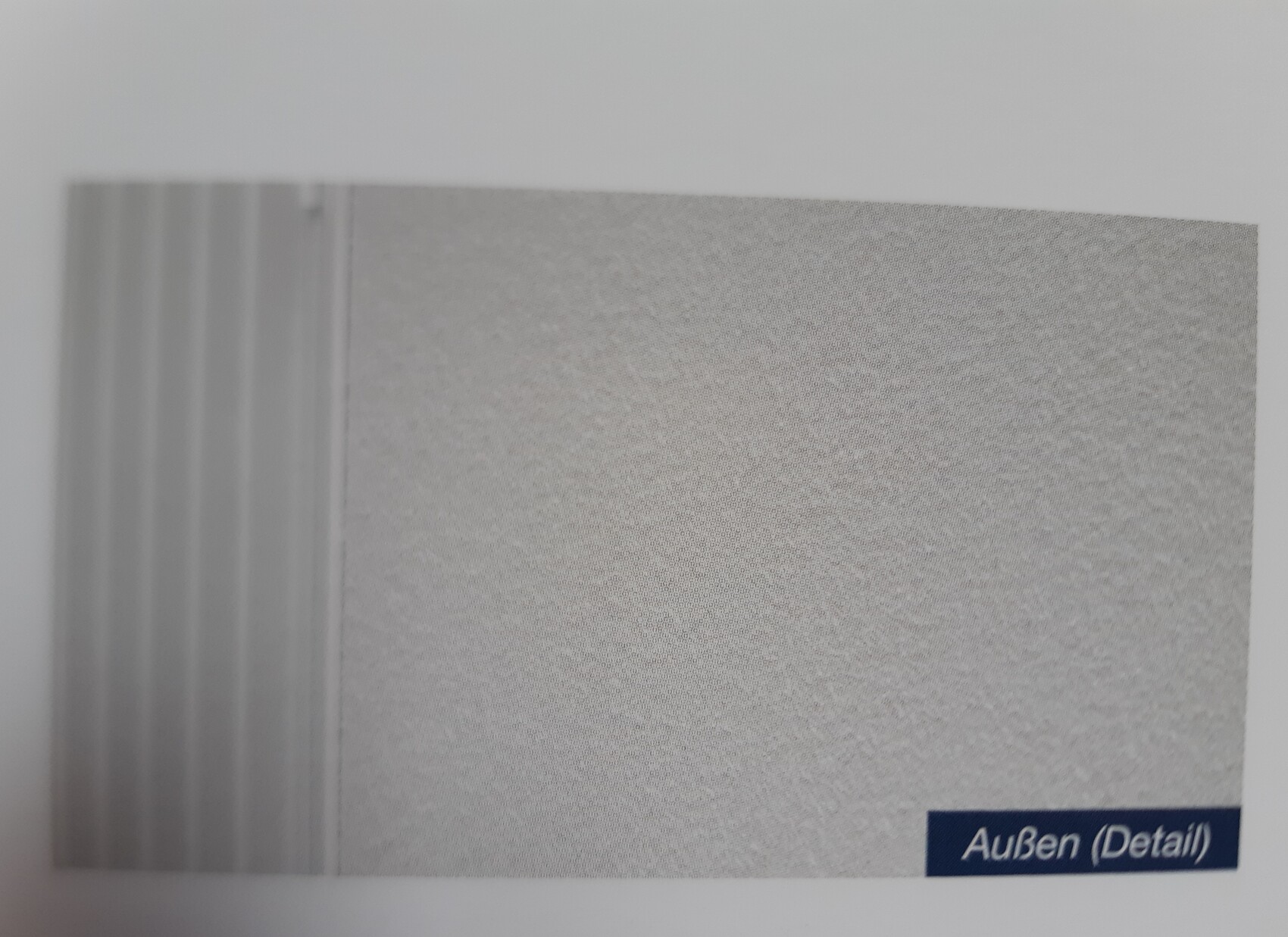 Nahaufnahme einer hellgrauen, texturierten Wand mit vertikalen Linien links; Außen (Detail)