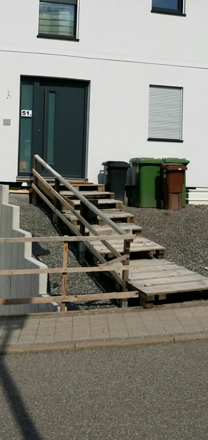 Weißes Wohnhaus mit dunkler Tür, Holzpaletten-Treppe und Mülltonnen vor Eingang 51