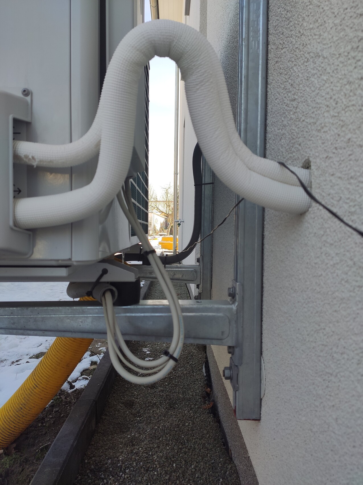 Außen-Klimagerät an der Hauswand mit isolierten Schläuchen und Kabeln