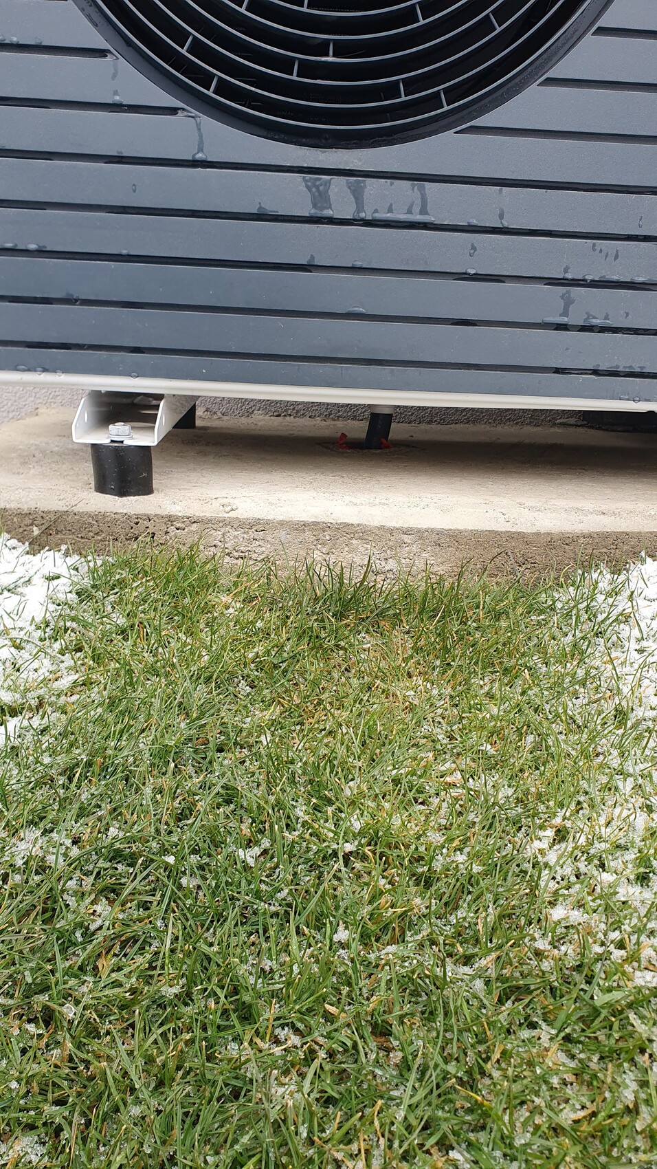 Außengerät einer Klimaanlage/Kondensator auf Stützen, Grasboden mit Schnee.