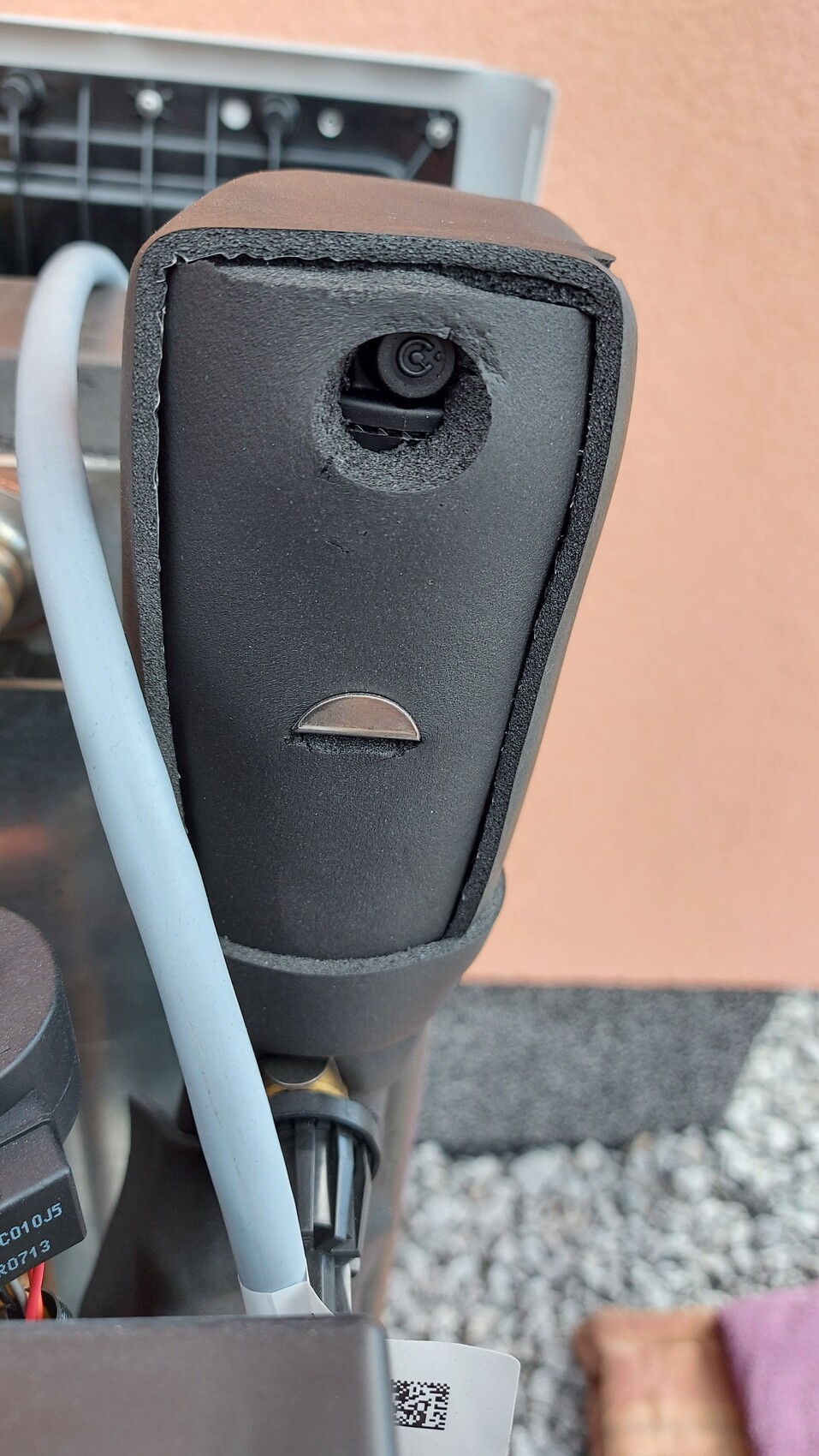 Nahaufnahme eines beschädigten schwarzen Gehäuses mit runder Öffnung und grauem Kabel